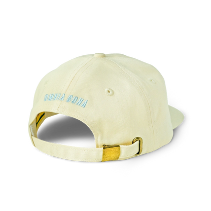Rear view of cream-colored Omnia Bona baseball cap featuring light blue logo embroidery and gold-tone adjustable strap