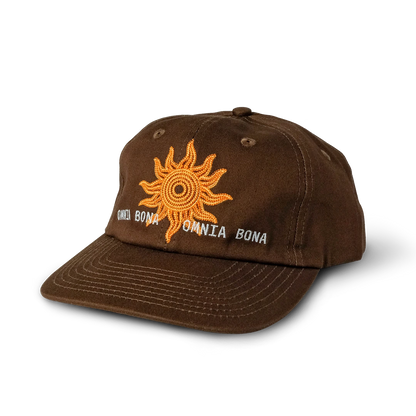 Brown baseball cap featuring embroidered orange sun design and white “OMNIA BONA” text – premium streetwear accessory