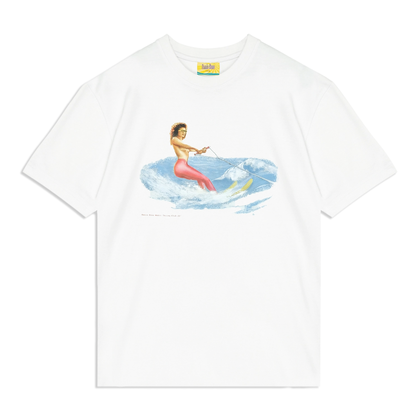 White graphic T-shirt featuring a vintage-style illustration of a woman in red pants and high heels water skiing on blue waves while holding a tow rope, with the text 'Omnia Bona Water Skiing Club '87' below the design.