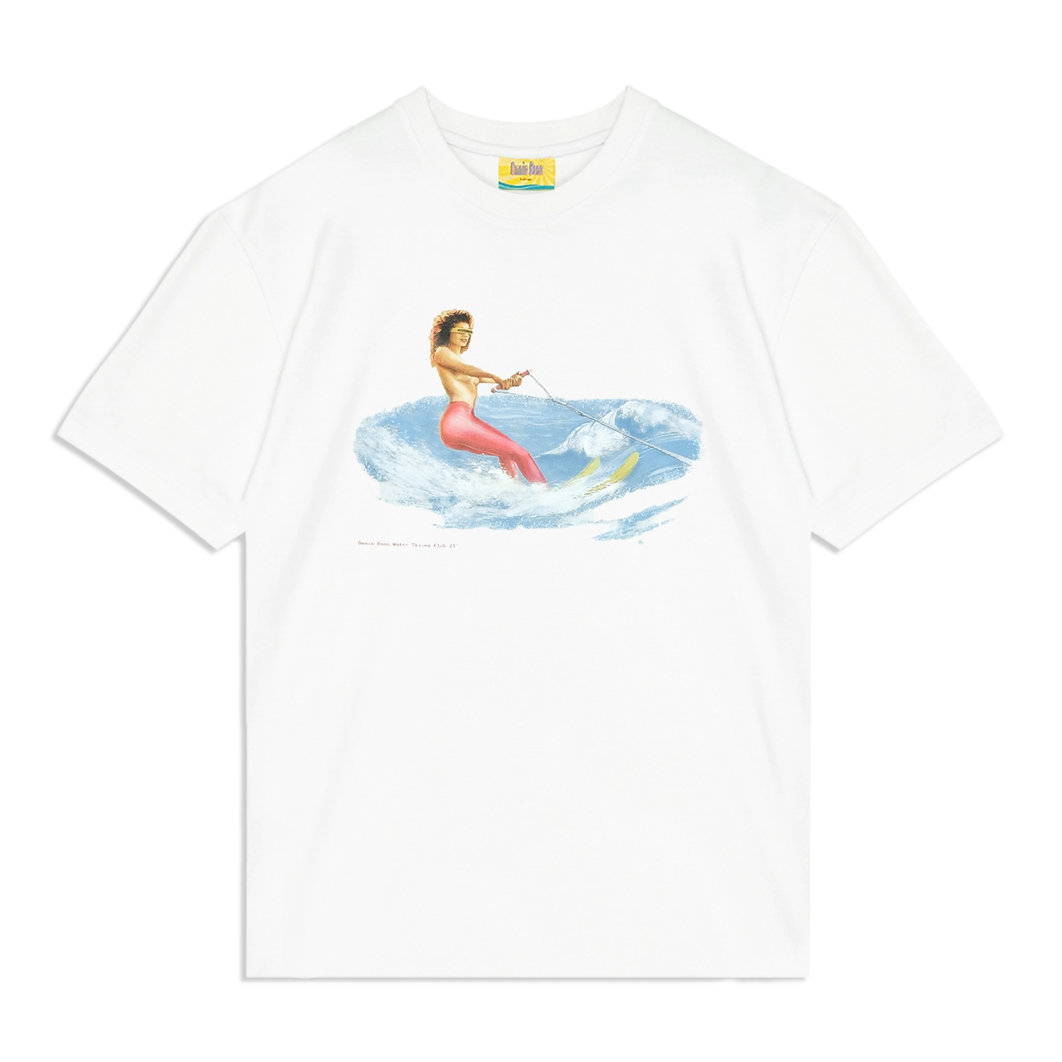 White graphic T-shirt featuring a vintage-style illustration of a woman in red pants and high heels water skiing on blue waves while holding a tow rope, with the text 'Omnia Bona Water Skiing Club '87' below the design.